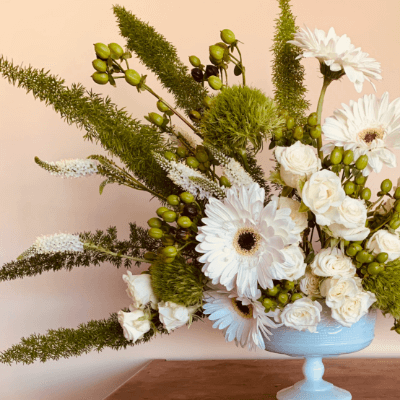 A white and green arrangement in a blue vase.